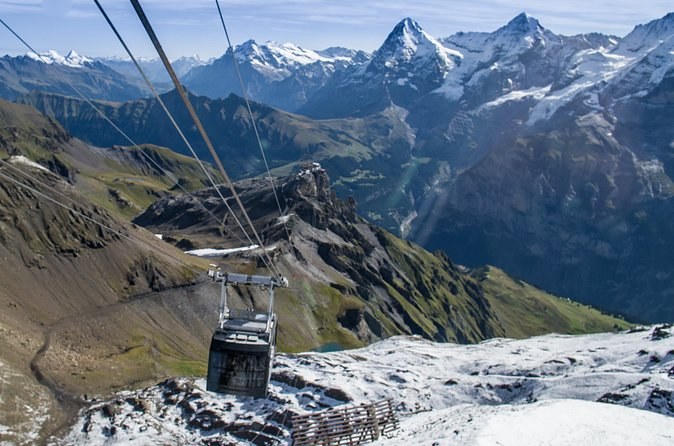 A cable car hanging above a deep valley, three snow peaks on the far skyline