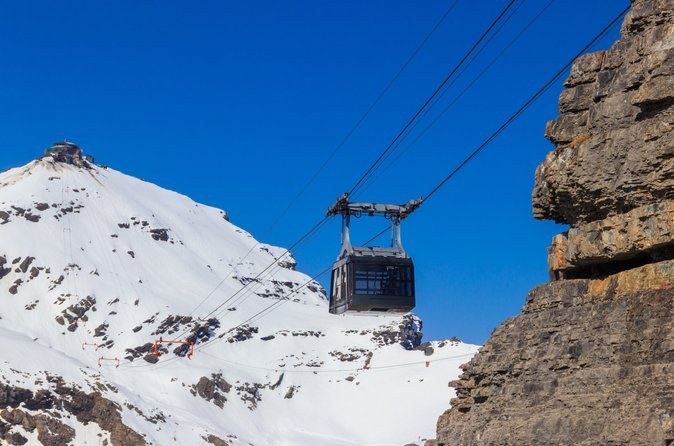 A cable car cabin rising towards a round summit building on a snowy crest