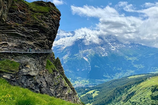 A steel walkway clinging to a layered rock outcrop high above a green valley