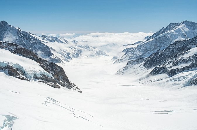 A broad glacier filling a high valley between snow-covered peaks under a clear sky