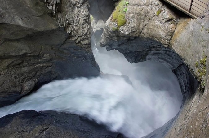 Grey glacier water swirling white through a round bowl worn into the rock