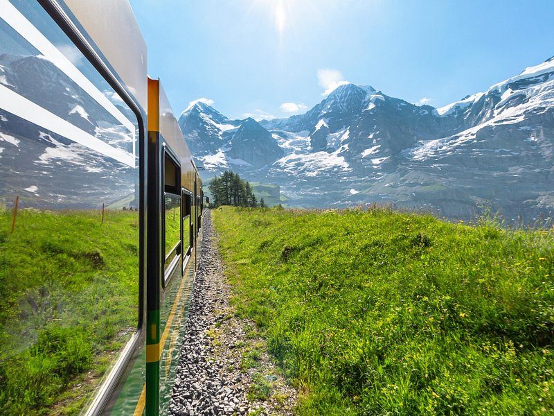 The view from a mountain train window: a green slope and snowy peaks ahead