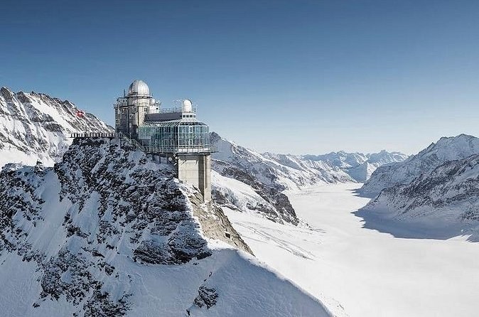 A domed observatory on a ridge above a long glacier curving between snowy peaks