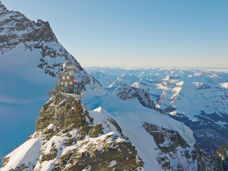 A domed observatory on a rocky spur high above snowfields and a sea of peaks