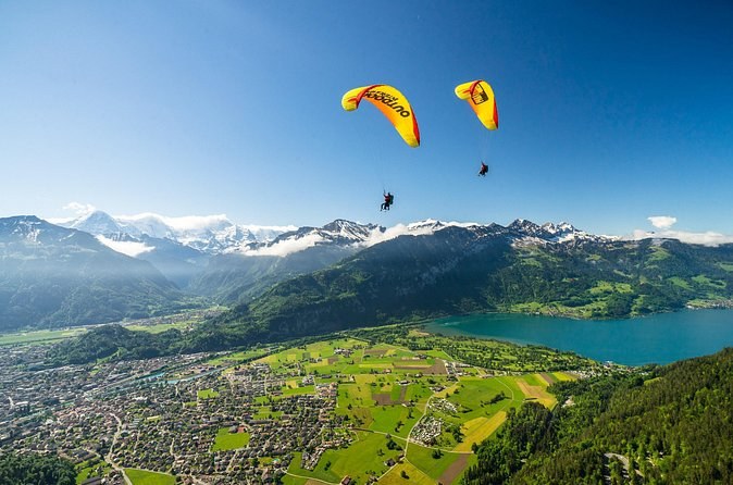 Two paragliders over a wide valley, a town and a turquoise lake far below