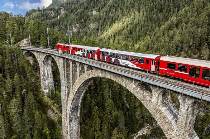 A red train crossing a tall curved stone viaduct above a wooded gorge