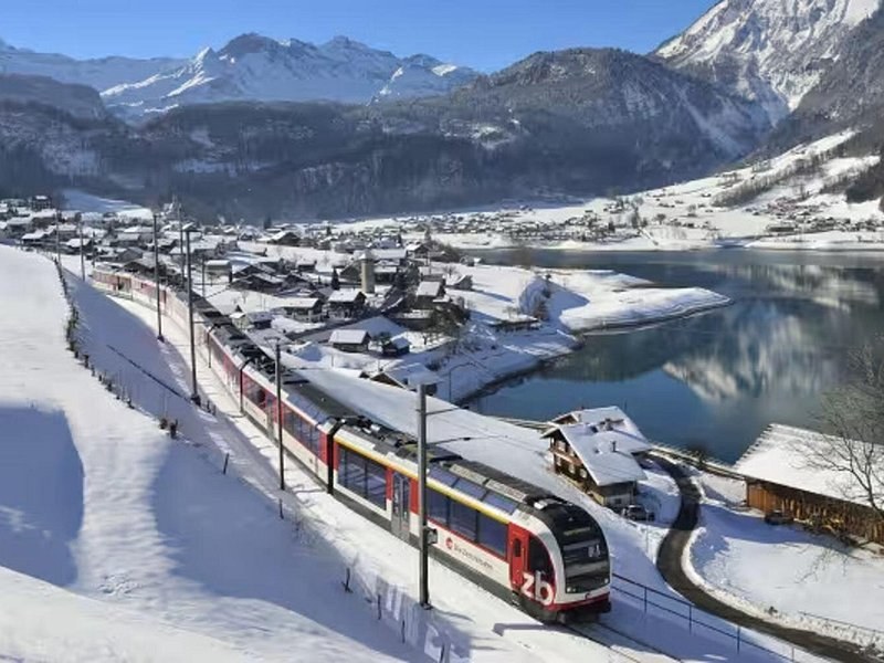 A red and white train curving through a snow-covered village in winter