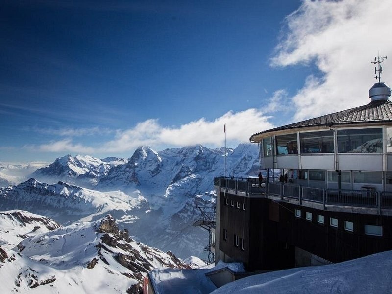 A round summit restaurant with a flat roof beside a sea of snowy peaks