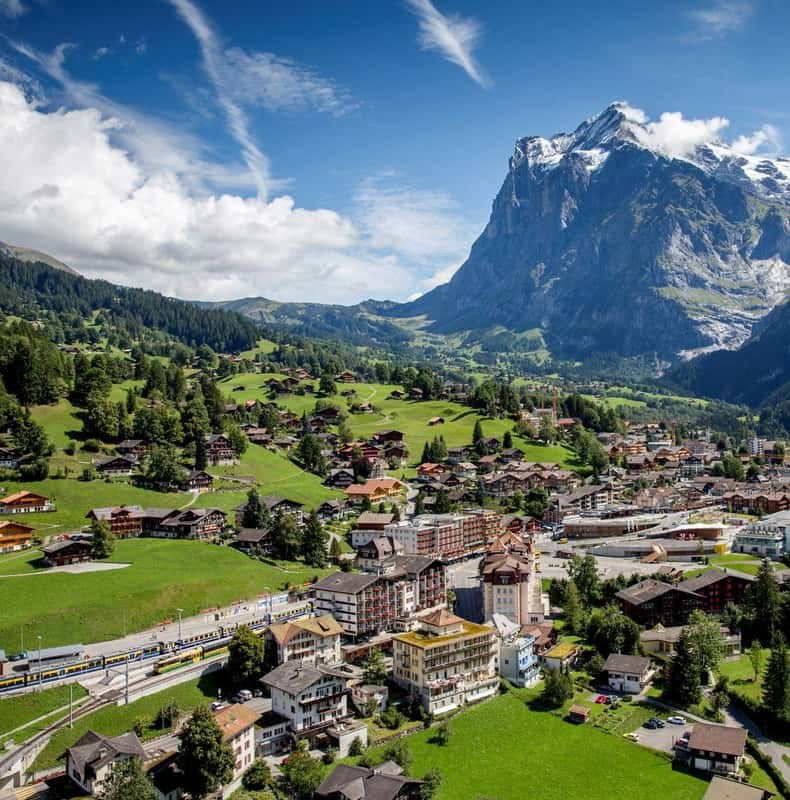A village of chalets spread across meadows below a sheer rock peak