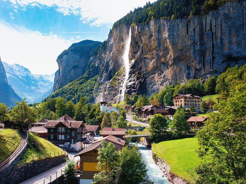 A valley village and a river below a free-falling waterfall off a limestone wall